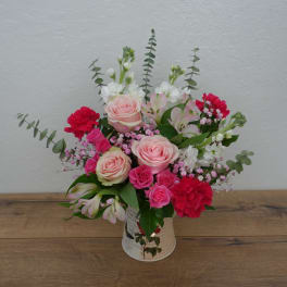 Pink and red mixed flower arrangement in a decorative tin container