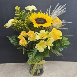 Yellow floral arrangement with a sunflower and roses in a glass vase