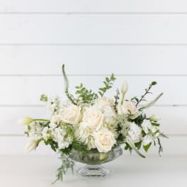 White roses and tulips arranged in a clear glass compote vase