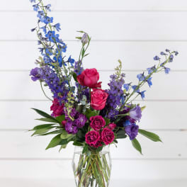 Mixed bouquet of pink roses and blue-purple flowers in a clear glass vase