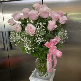 Pink roses in a glass vase with baby's breath and a pink ribbon
