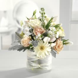Low arrangement of white and peach flowers in a frosted glass vase wrapped with a sheer ribbon