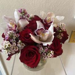 Red roses with white orchids in a clear glass vase