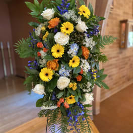 Standing floral spray with yellow daisies, white roses, and blue flowers