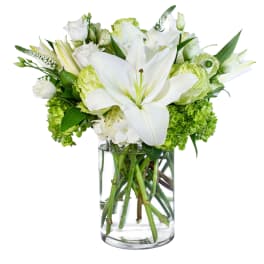 White lilies and green blooms arranged in a clear glass vase