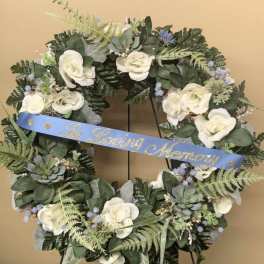 White floral memorial wreath with a blue ribbon on a stand