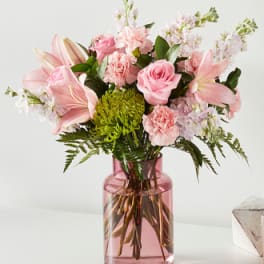 Pink bouquet of lilies, roses, and carnations in a pink glass vase