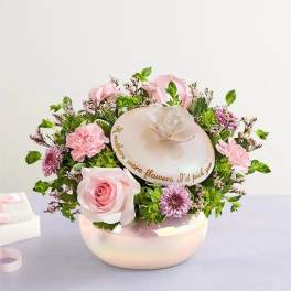 Pink roses and carnations arranged in a round hat box with a decorative lid