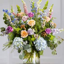 Mixed bouquet of roses, hydrangeas, and blue delphinium in a glass vase