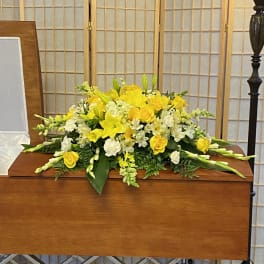 Yellow and white floral casket spray on a wooden casket