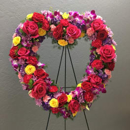Heart-shaped floral wreath on a stand with red, pink, yellow, and purple flowers