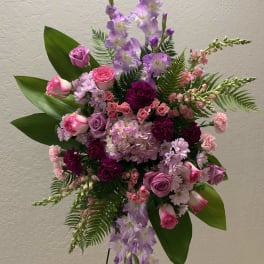 Standing floral spray with pink and purple flowers on a black easel
