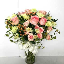 Pink roses and pale green carnations in a glass vase with a white ribbon