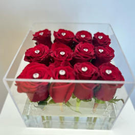 Red roses arranged in a clear acrylic box with small gem accents