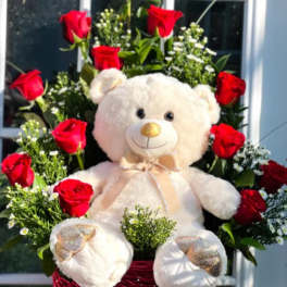 Red roses arranged around a teddy bear in a basket