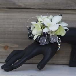 White floral wrist corsage with black and silver ribbon on a black hand display