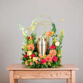 Floral urn arrangement with orange gerberas, roses, and a silver urn