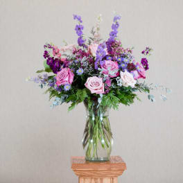 Tall arrangement of pink roses and purple flowers in a clear glass vase