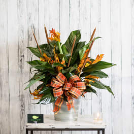 Autumn arrangement with green tropical leaves and orange accents in a silver vase