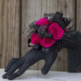 Hot pink rose wrist corsage with black glitter ribbon displayed on a black mannequin hand.