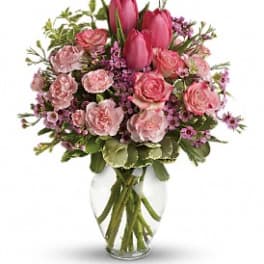 Pink tulips, roses, and carnations in a clear glass vase with small purple filler flowers