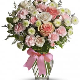Pastel bouquet of pink and white roses, carnations, and mums in a clear glass vase with a pink bow.