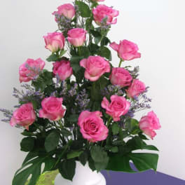 Tall arrangement of pink roses with purple filler flowers in a white vase