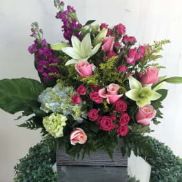 Tall arrangement of pink roses, white lilies, and hydrangeas in a rectangular gray container