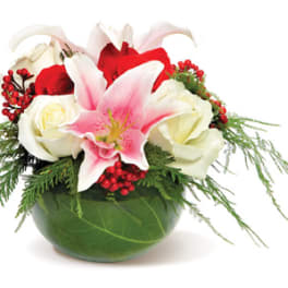 Low arrangement of pink lilies, red and white roses, and red berries in a green bowl vase
