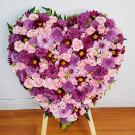 Heart-shaped floral arrangement of pink and purple blooms on an easel