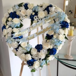 Heart-shaped floral wreath with white, blue, and pale blue flowers on an easel