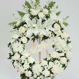 White funeral wreath with roses and lilies on a wooden easel