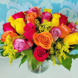 Vibrant bouquet of multicolored roses with yellow filler flowers in a clear glass vase