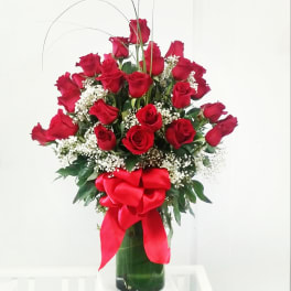 Red roses arranged in a tall glass vase with a red bow