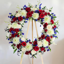 Heart-shaped floral wreath with red, white, and blue flowers on a wooden stand