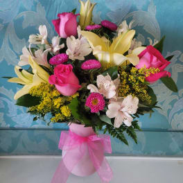 Bouquet of pink roses, lilies, and mixed flowers in a pink vase with ribbon