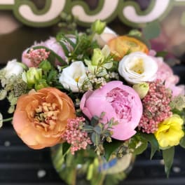 Mixed pastel bouquet with peonies, ranunculus, and small blooms in a glass vase