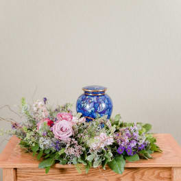 Low floral arrangement with pink and purple roses around a blue urn
