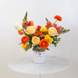 Bright mixed bouquet in a white vase with orange, yellow, and cream flowers