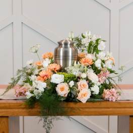 Floral funeral urn arrangement with peach, white, and pink flowers