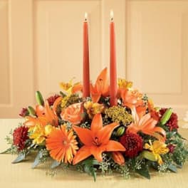 Orange floral centerpiece with two red taper candles