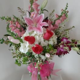 Pink and white mixed bouquet in a clear glass vase with a pink ribbon
