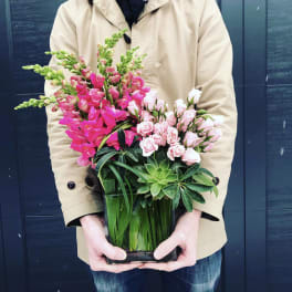 Pink flowers and succulents arranged in a square glass vase