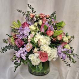Large mixed arrangement of pink roses, white hydrangeas, lavender blooms and lilies in a clear glass vase