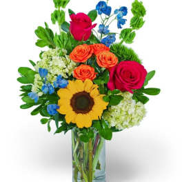 Mixed bouquet in a clear glass vase with roses, sunflower, and blue flowers