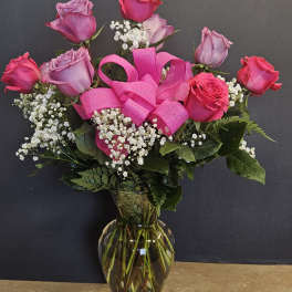 Pink and lavender roses in a glass vase with a bright pink ribbon