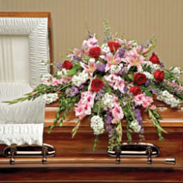 Casket spray of red roses, pink lilies, and mixed flowers on a wooden casket