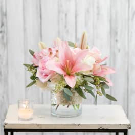 Pink lilies and roses in a glass vase beside a lit candle