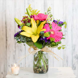 Bright mixed bouquet in a glass vase with a candle beside it