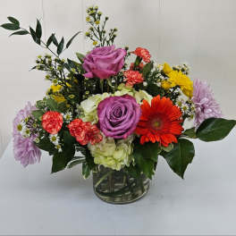 Mixed bouquet with purple roses, gerbera daisy, carnations, and hydrangea in a glass vase